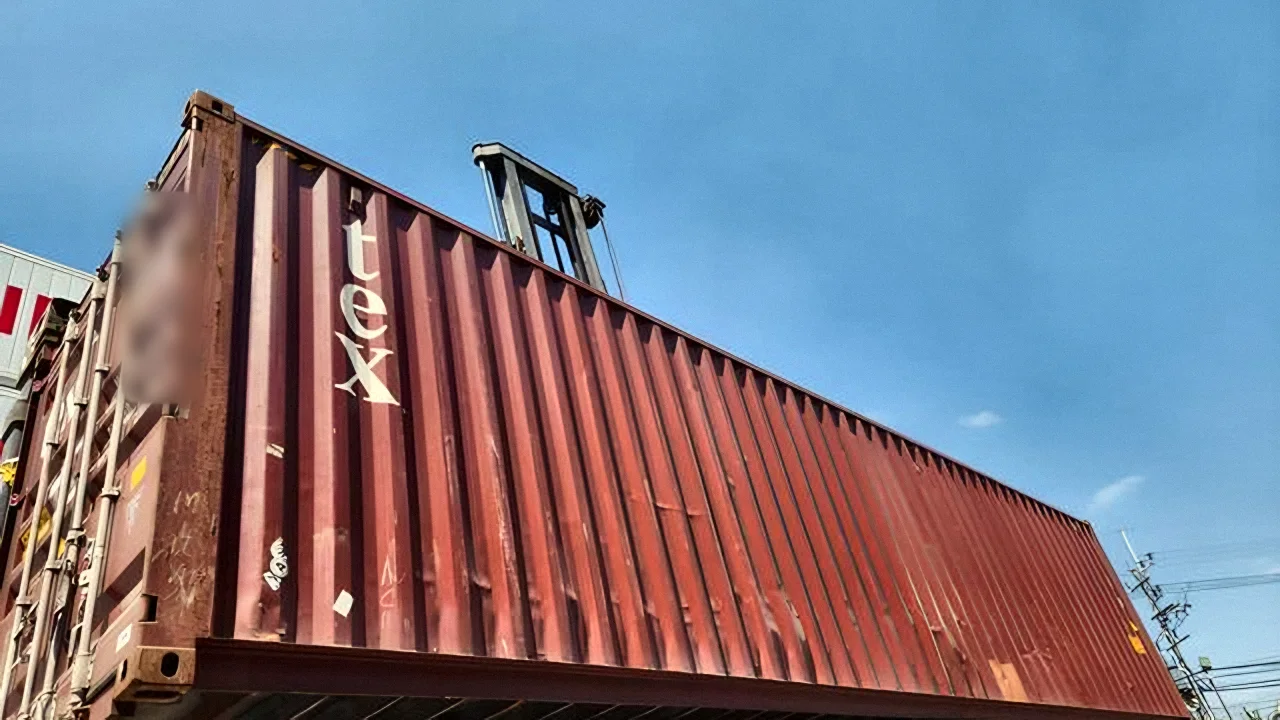 An empty 40-foot container lifted onto a truck under a clear sky
