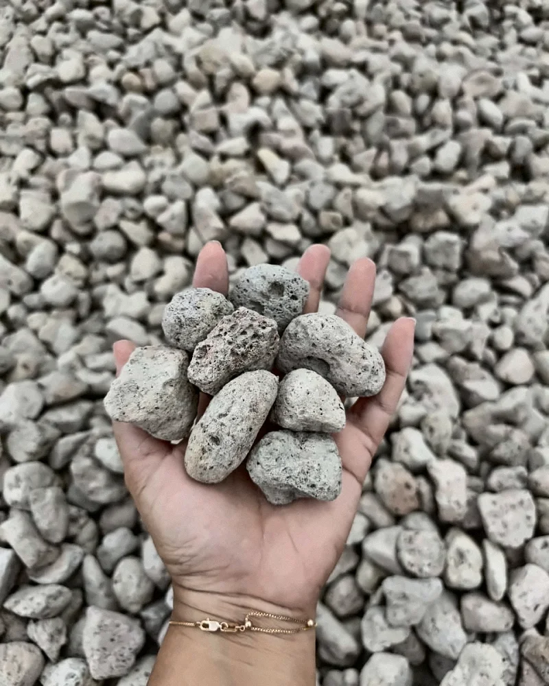 A hand holding several pumice stones above a large pile of pumice